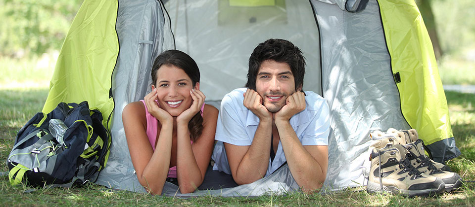 Smiling couple is looking out of their tend while relaxing in a campsite 