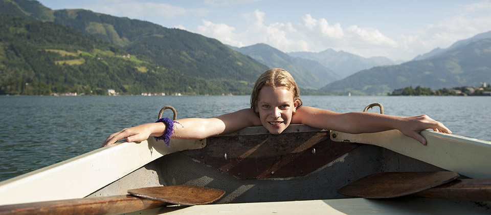 In the middle of the Lake of Caldaro a girl is trying to enter her boat after swimming