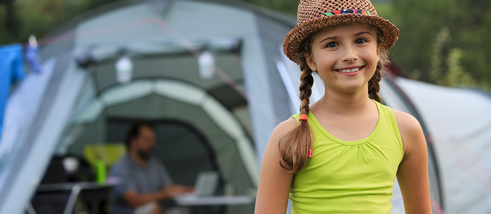 A happy smiling girl with straw-hat in front of a tend in a campsite in Val Venosta