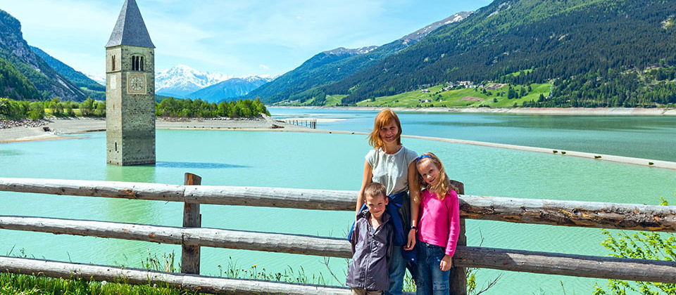 A mother and her kids in front of the partially sunken bell tower of Curon Venosta