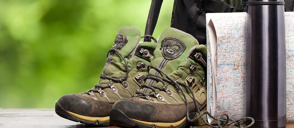 Dettaglio di scarpe da montagna, una cartina, uno zaino e una borraccia