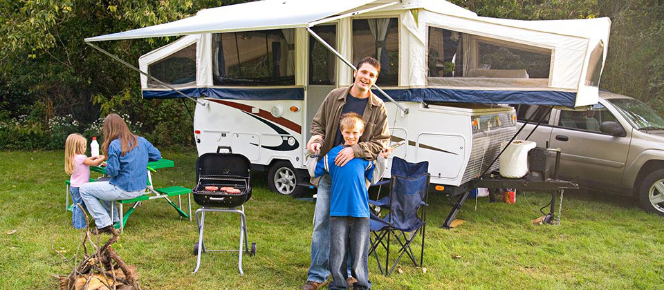 Eine Familie in Südtirol in der Nähe eines Waldes beim Grillen vor ihrem Wohnwagen