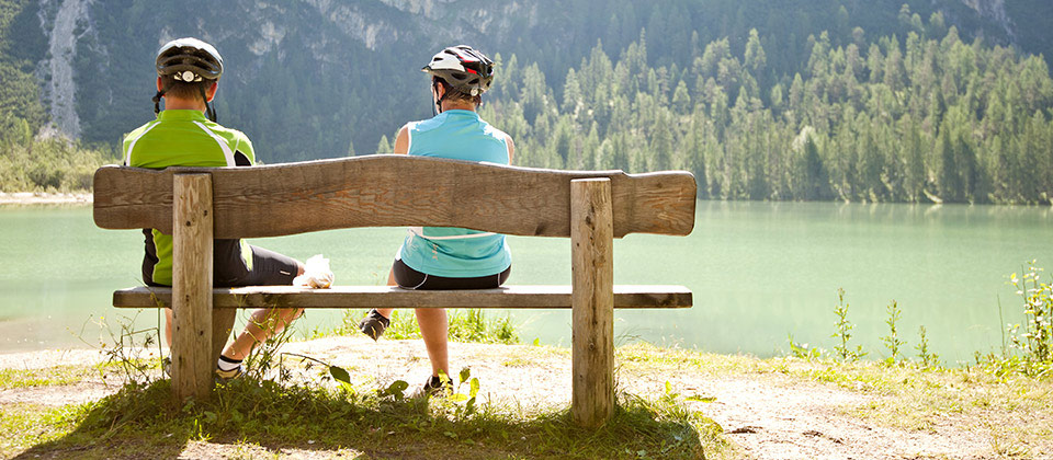 Cyclists in South Tyrol regaining breath by sitting on a wooden bench in front of a lake