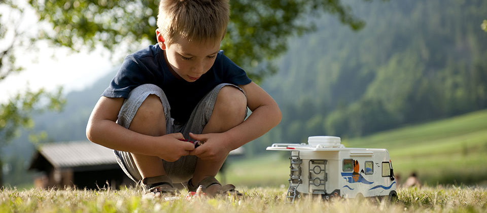 A small boy playing with a toy camper van in the mountains of South Tyrol